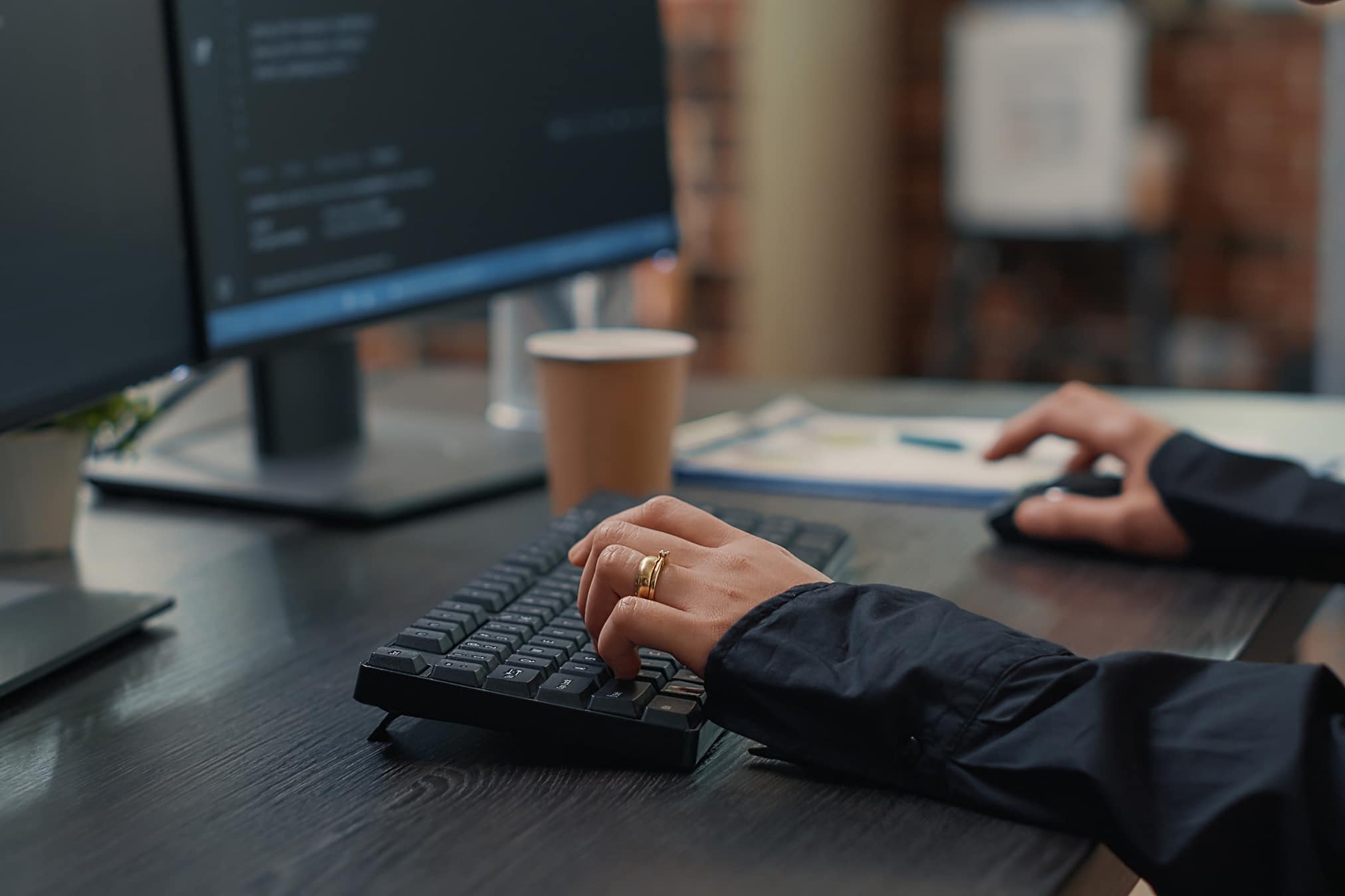 Closeup of developer hands typing code on keyboard while looking at computer screens with programming interface. Software programmer sitting at desk with clipboard writing algorithm.